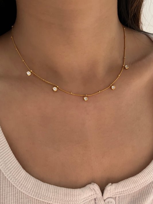 Gold necklace with small pendants on a person wearing a light pink top.