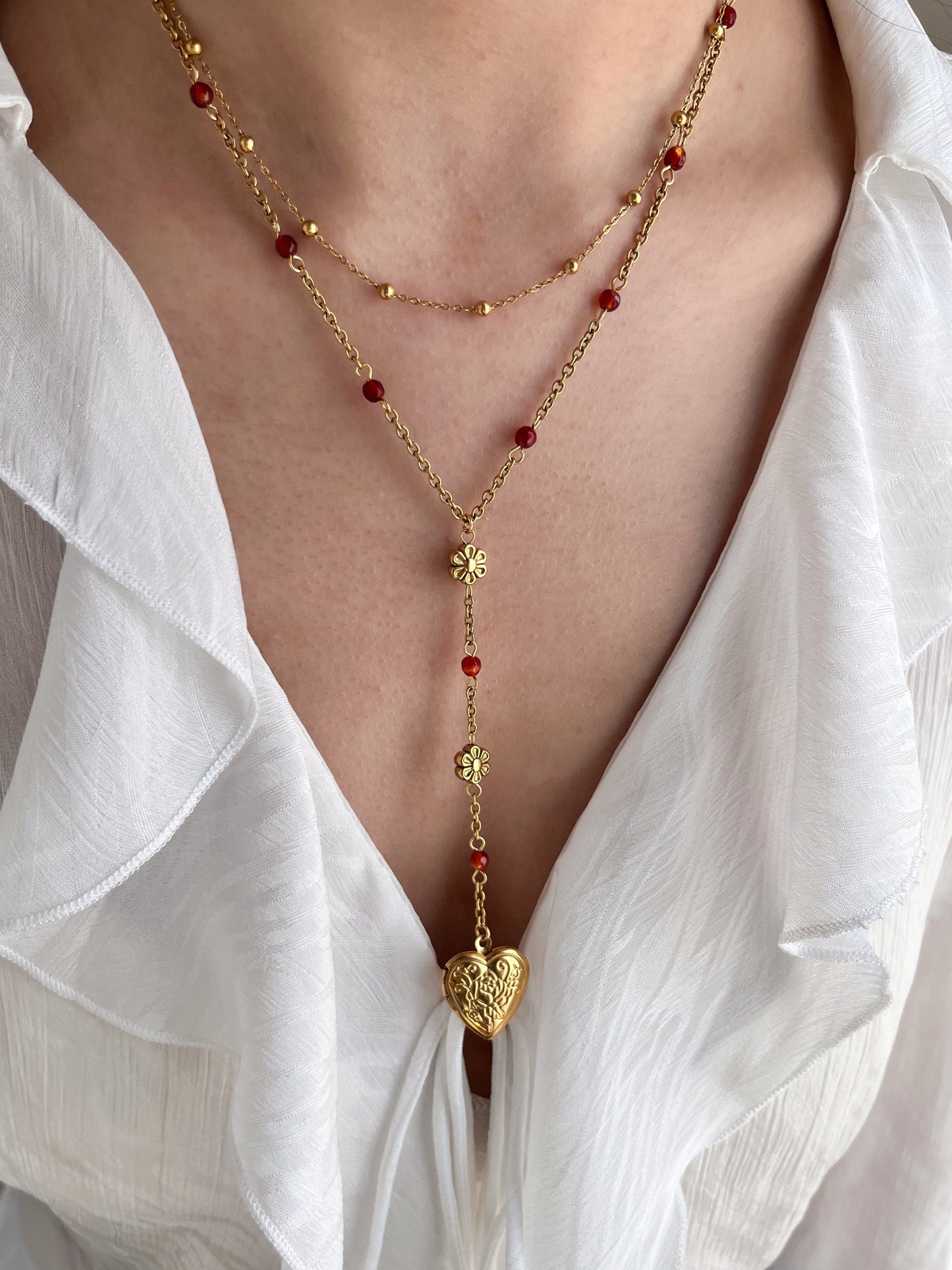 Gold necklace with red beads worn by a person in a white shirt