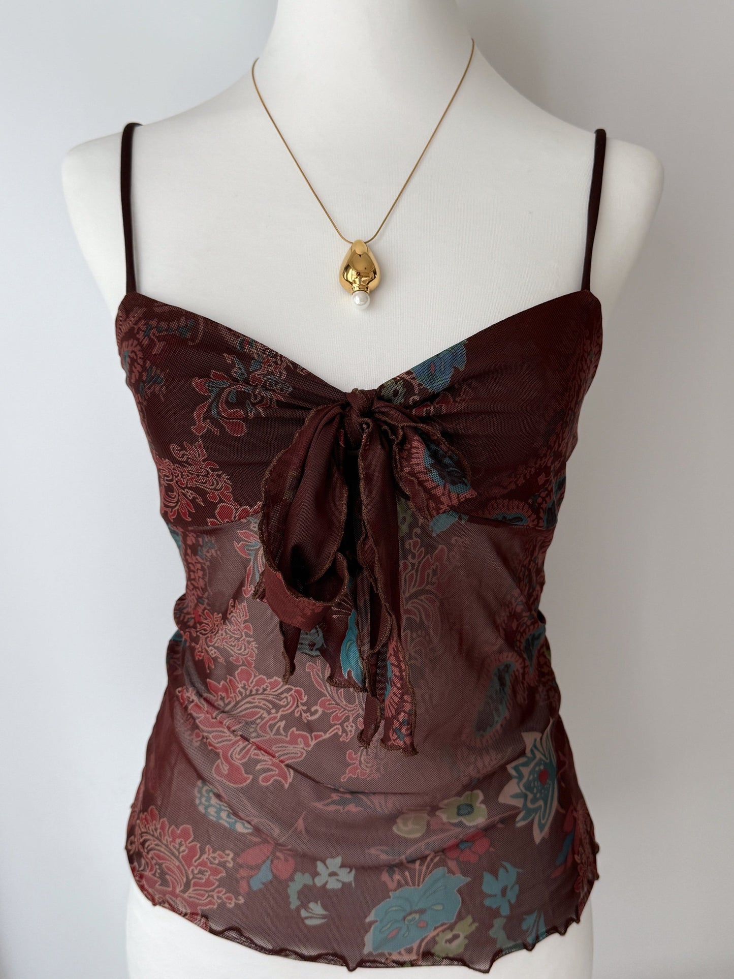 Brown patterned top on a mannequin with a gold necklace against a white background