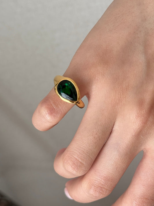 Gold ring with a green gemstone on a finger against a neutral background