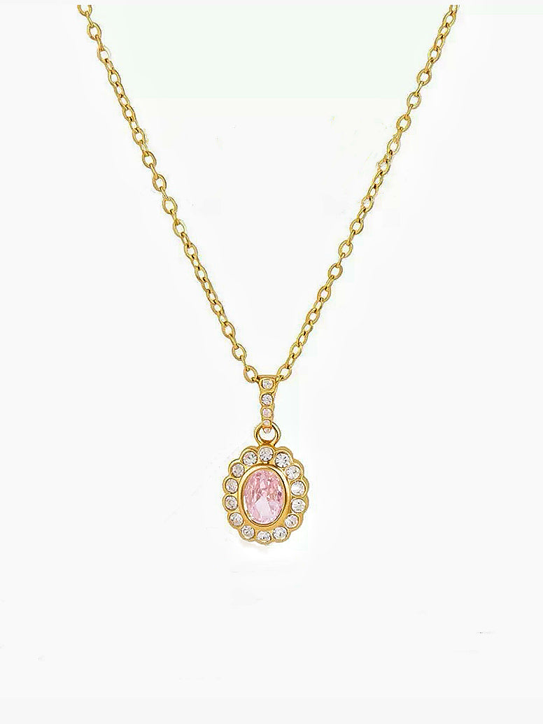 A gold chain necklace with an oval pendant featuring a pink cabochon gemstone surrounded by small clear stones, set against a plain white background.