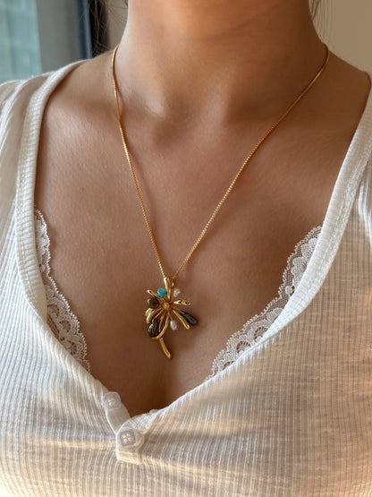 A gold chain necklace with a dragonfly pendant featuring turquoise and white accents, worn by a model in a white ribbed top.
