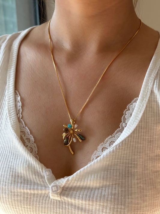 A gold chain necklace with a dragonfly pendant featuring turquoise and white accents, worn by a model in a white ribbed top.