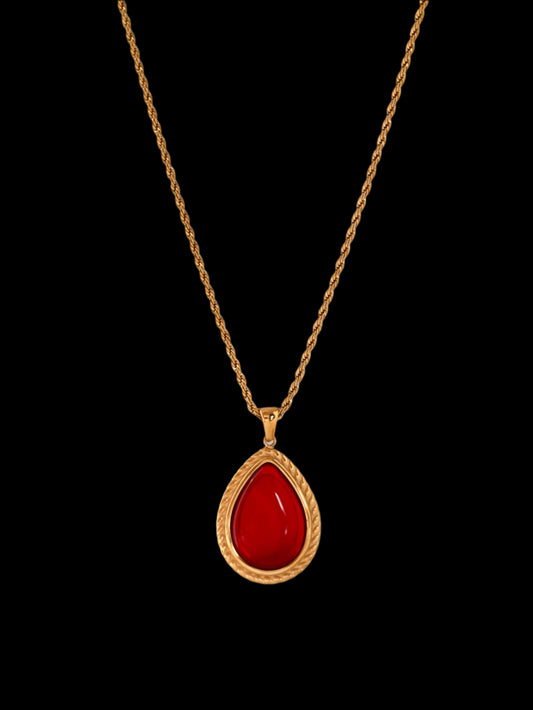 Gold necklace with a red teardrop pendant on a white background