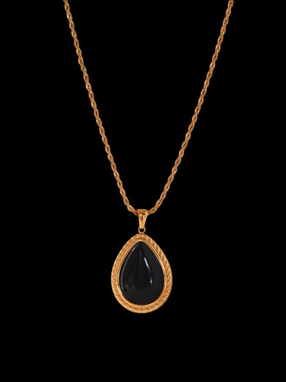 Necklace with a black teardrop pendant on a gold chain against a white background
