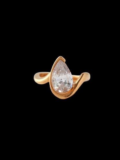 Gold ring with a clear teardrop-shaped gemstone on a light gray background