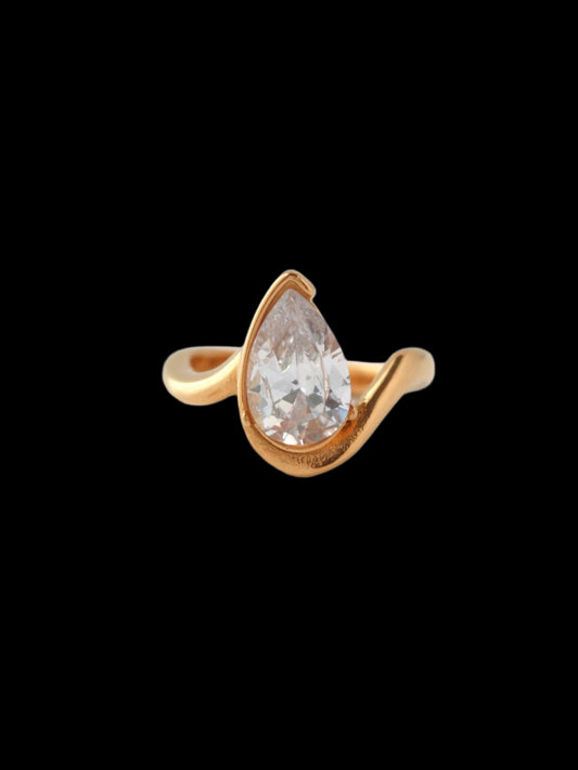Gold ring with a clear teardrop-shaped gemstone on a light gray background