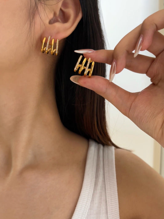 Gold hoop earrings being worn and held by a hand against a neutral background