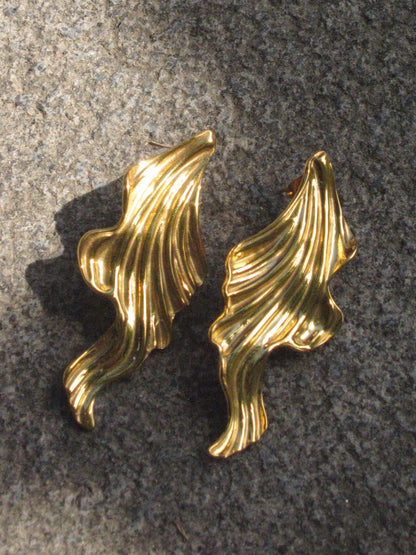 Pair of gold leaf-shaped earrings on a textured gray surface