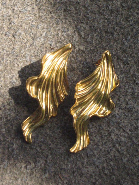 Pair of gold leaf-shaped earrings on a textured gray surface