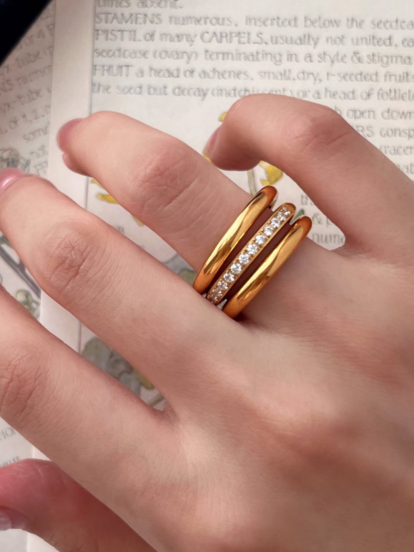 Hand wearing two gold rings on a textured surface with text