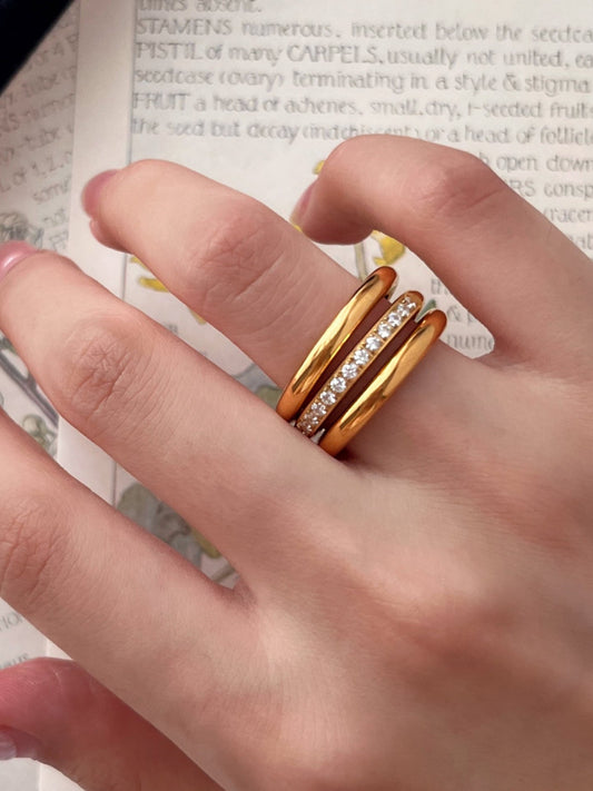 Hand wearing two gold rings on a textured surface with text