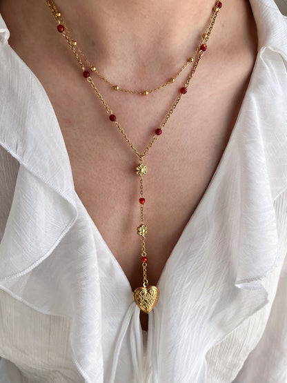 Gold necklace with red beads worn by a person in a white shirt