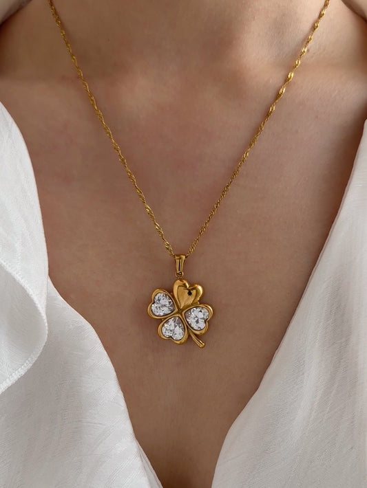 Gold necklace with a clover-shaped pendant worn by a person in a white shirt.
