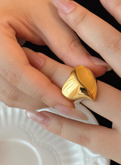Gold ring being worn on a finger with a white dish in the background