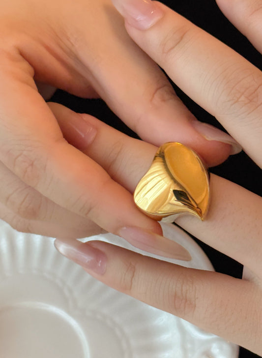 Gold ring being worn on a finger with a white dish in the background