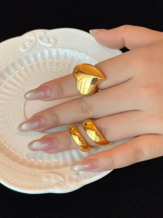 Hand wearing gold leaf-shaped rings on a decorative plate with a black background