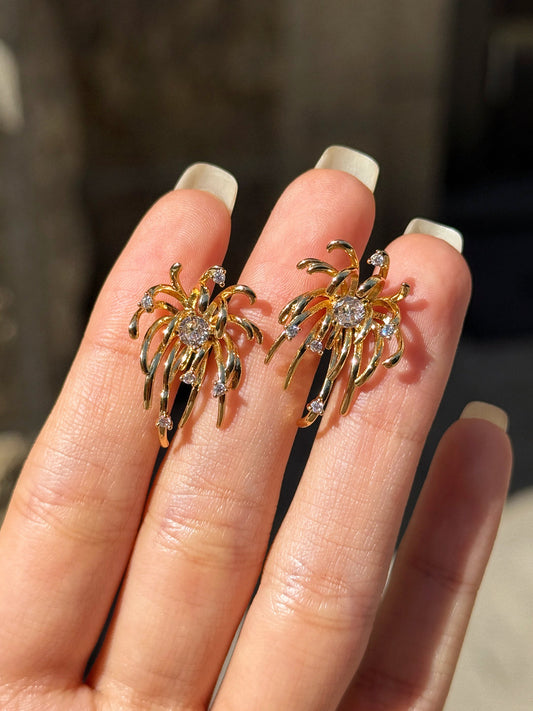 Gold spider-shaped earrings on a hand with a blurred stone wall background