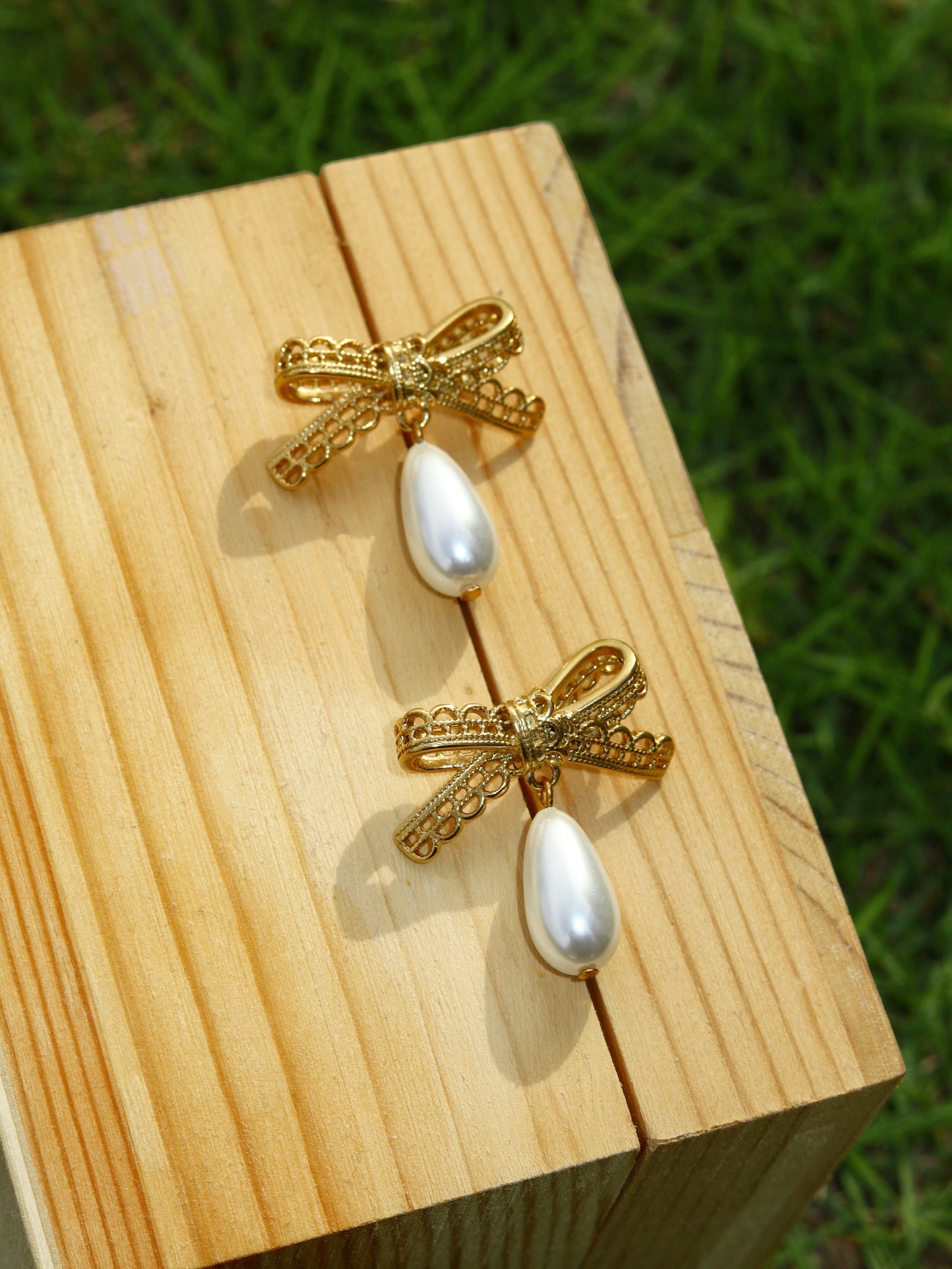 Gold bow-shaped earrings with pearl-like centers on a wooden block.