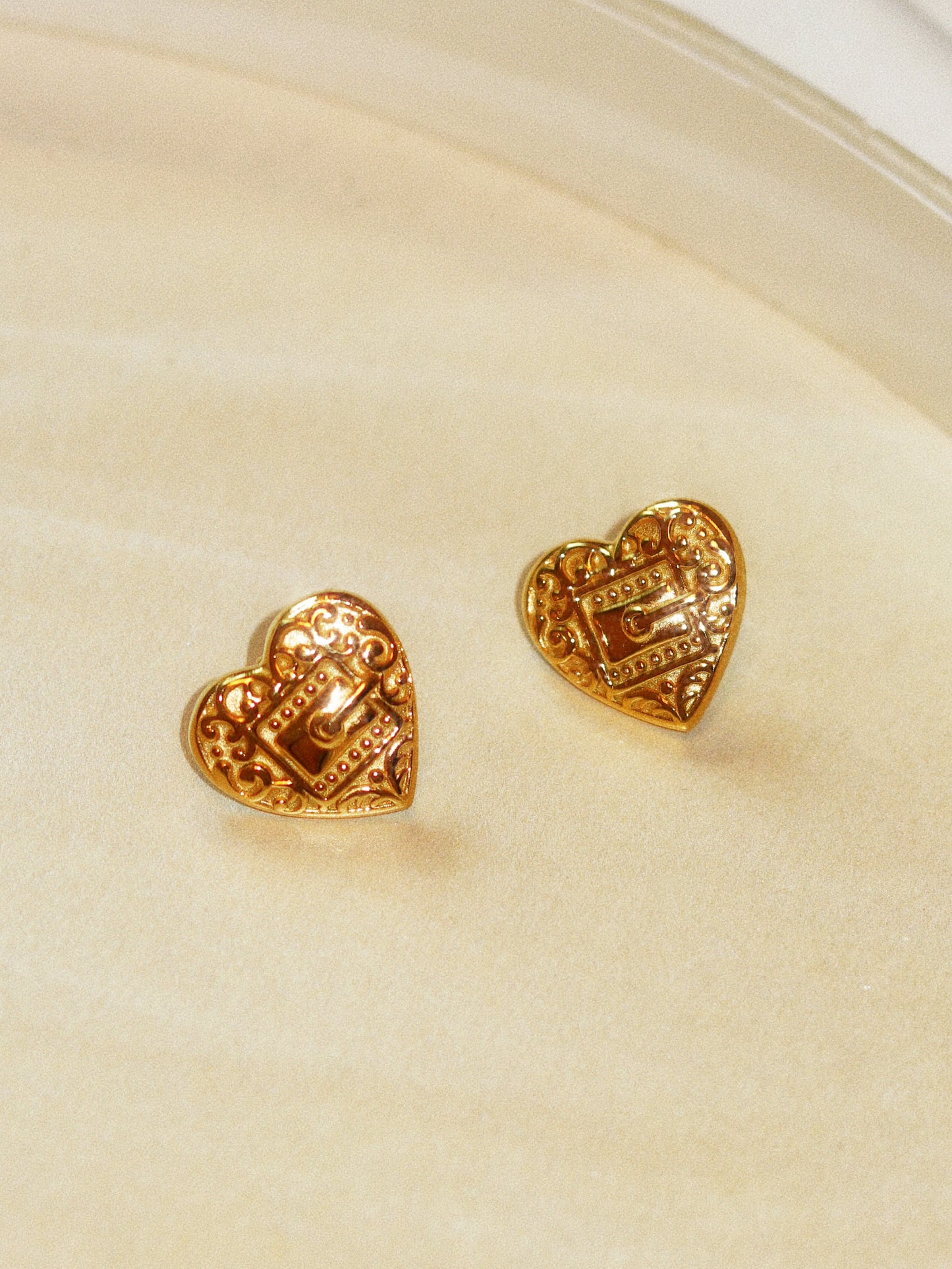 Gold heart-shaped earrings on a beige background