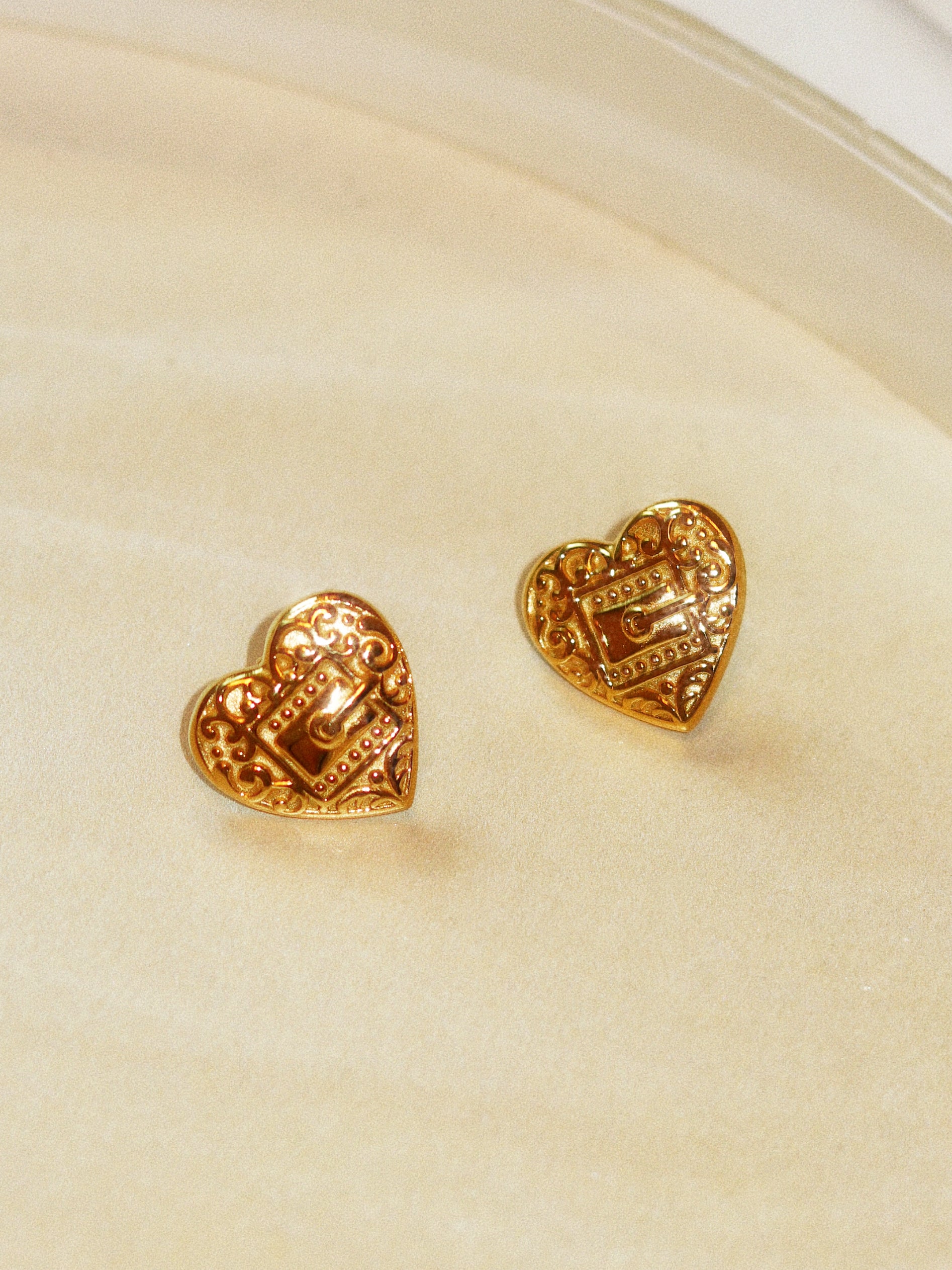 Gold heart-shaped earrings on a beige background