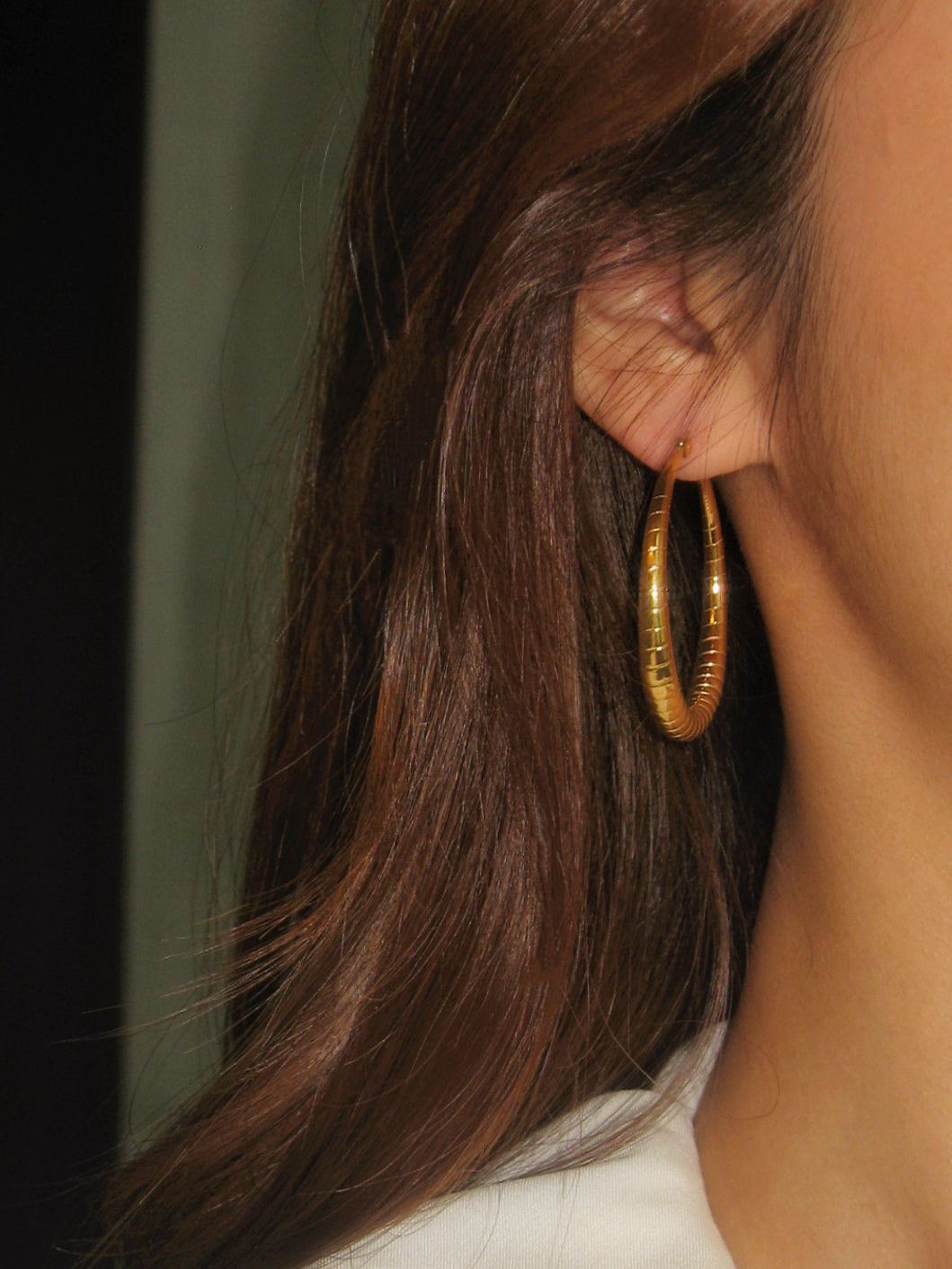 Close-up of a person wearing a gold hoop earring with hair partially covering the face.
