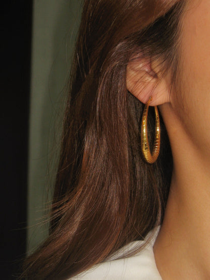 Close-up of a person wearing a gold hoop earring with hair partially covering the face.