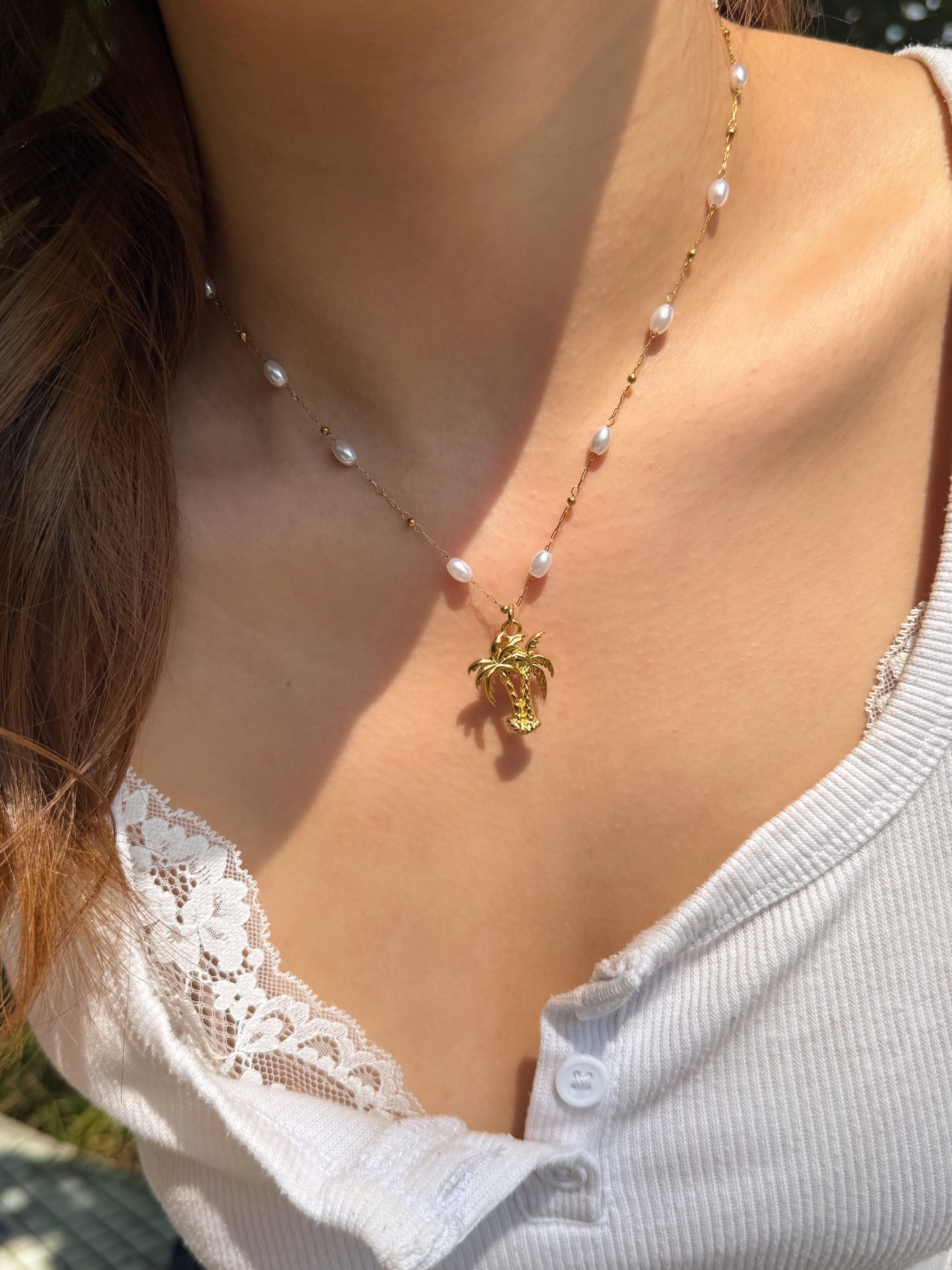 A close-up of a woman wearing a delicate gold necklace with small white pearls and a gold turtle pendant, styled with a white lace-trim top.