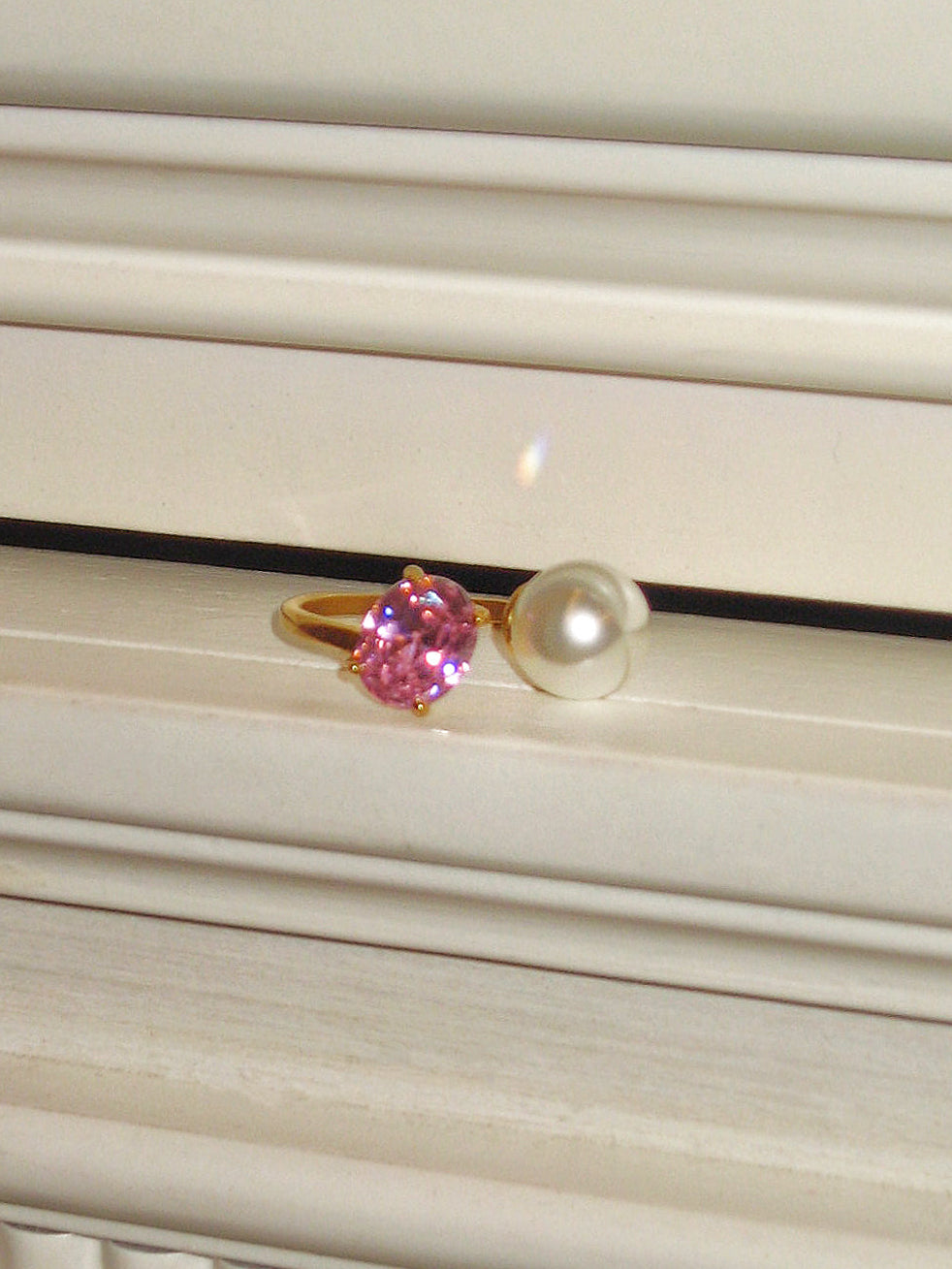 Ring with pink gemstone and pearl on a textured surface