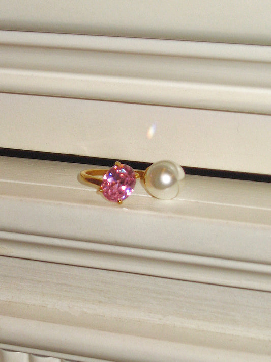 Ring with pink gemstone and pearl on a textured surface