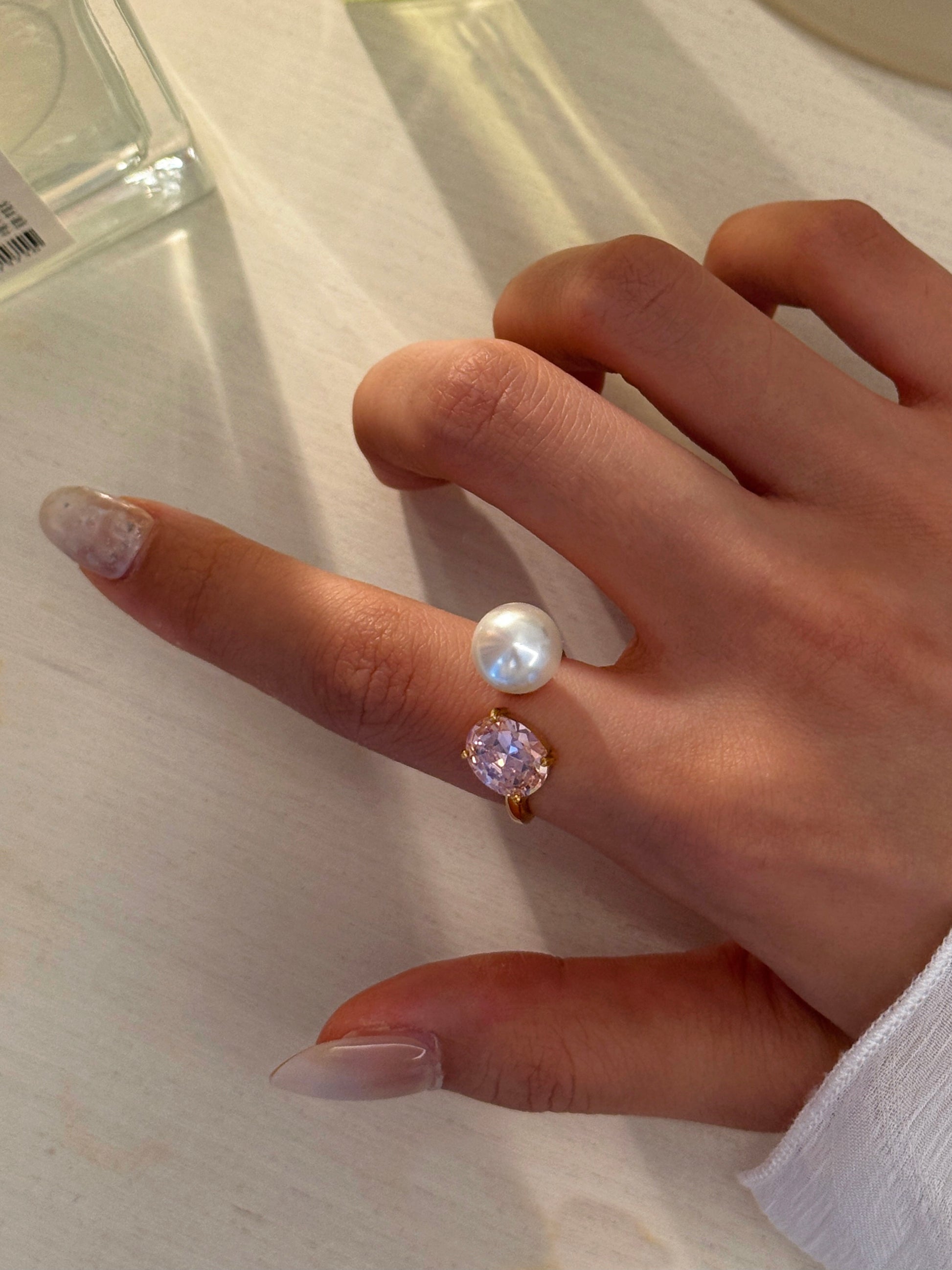 Hand wearing a ring with pearls and a pink gemstone on a light background